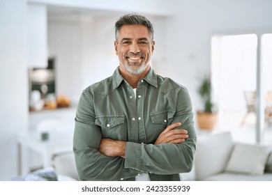 Happy confident middle aged senior man standing with arms crossed at home. Smiling older mature 50 years old handsome man looking at camera posing in modern house living room. Portrait.