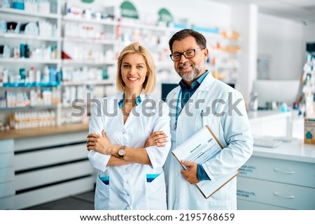 Happy confident pharmacist and her mature coworker working in pharmacy and looking at camera.