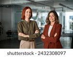 Happy confident professional business women of young and middle age posing at work looking at camera. Two smiling confident ladies standing arms crossed in office. Women power partnership, portrait.