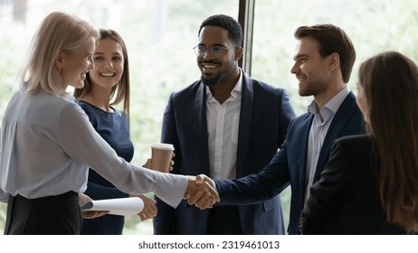 Happy confident senior businesswoman, business leader, coach getting acquainted with new team of employees, interns, students, standing and shaking hands with worker at informal meeting - Powered by Shutterstock