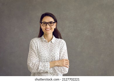Happy confident smiling caucasian woman looking at camera studio headshot portrait. Casual positive lady showing cheerful emotion sanding on grey background. Feminine and youth, people expression
