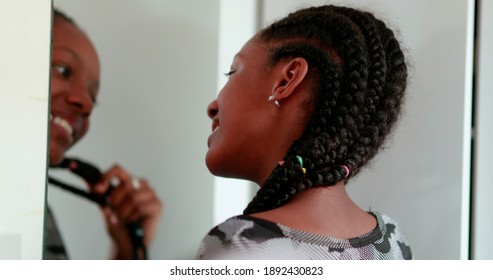 Happy confident teen black girl standing by mirror reflection smiling and playing with hair