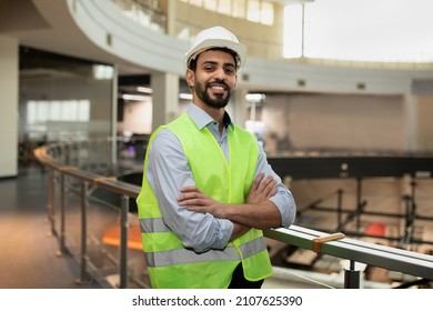 Happy confident young attractive arabic engineer in hard hat and protective clothing in office plant interior, free space. Professional work in industry, builder checking job at modern factory indoor