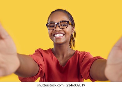 Happy Confident Young Black Woman Wearing Glasses Takes Selfie For Photo Or Video Blog. Positive Smiling Lady With Diastema Teeth Gap Holding Modern Cellphone In Both Hands On Yellow Colour Background