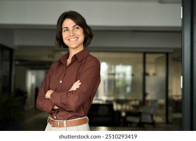 Happy confident young Hispanic professional business woman standing at work in office arms crossed looking away, proud businesswoman leader executive thinking of future career success. - Powered by Shutterstock