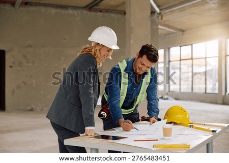 Happy construction worker going through blueprints with female building contractor on site.