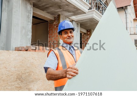Happy constructor standing outside behind empty cardboard with copy text space. Building a house of wood. Builder carries boards to construction site