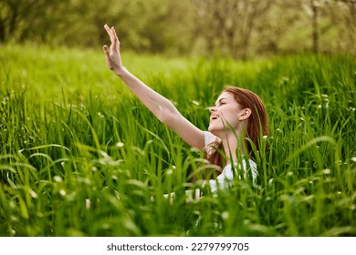 happy, contented woman sitting in tall green grass enjoying a pleasant day with her arms raised high - Shutterstock ID 2279799705
