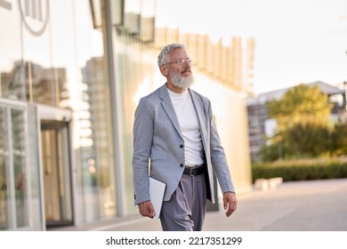 Happy Cool Bearded Stylish Old Mature Professional Business Man, Smiling Gray Haired Senior Older Businessman Wearing Suit Holding Tablet Walking Going Outdoors In Big City Business District Downtown.