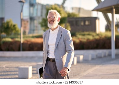 Happy Cool European Bearded Stylish Old Mature Professional Business Man, Smiling Gray Haired Senior Older Businessman Wearing Suit Holding Tablet Walking Going Outdoors In Big City On Sunny Day.