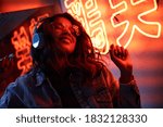 Happy cool fashion funky African young black hipster lady wears trendy glasses headphones listening dance pop dj music standing in neon night club light at style party. Translation: Chicken laugh