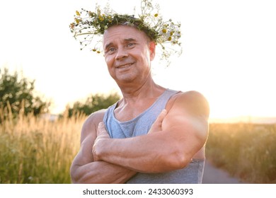 happy cool satisfied muscular funky hipster mature man of 60 years old smiles pretty in T-shirt in sunlight, cute wreath wildflowers, daisies on head, happiness in old age, connection with nature - Powered by Shutterstock