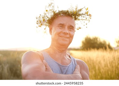 happy cool satisfied muscular funky hipster mature man of 60 years old smiles pretty in T-shirt in sunlight, cute wreath wildflowers, daisies on head, happiness in old age, connection with nature - Powered by Shutterstock