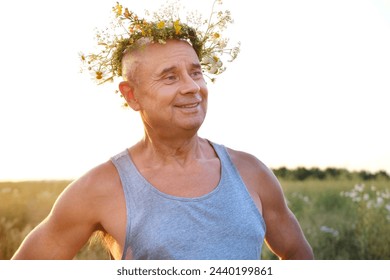 happy cool satisfied trendy funky hipster mature man of 60 years old smiles in T-shirt, cute wreath wildflowers, daisies, natural crown on head, image faun, satyr in sunlight, connection with nature - Powered by Shutterstock