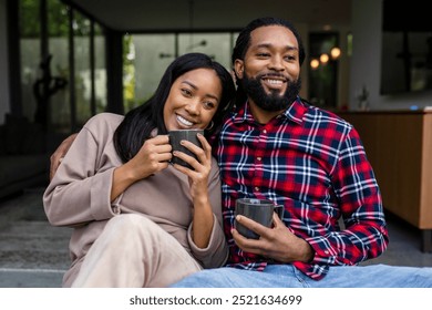 A happy couple, an African American man and a Black woman, enjoy coffee together. The couple smiles while holding mugs, love and connection in a cozy setting. African American couple drinking coffee. - Powered by Shutterstock