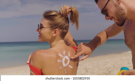 Happy couple applying sun tanning lotion on the beach, man putting sunscreen suntan cream on woman - Powered by Shutterstock