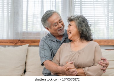 Happy couple Asian elder look at each other and embracing together on the sofa at home