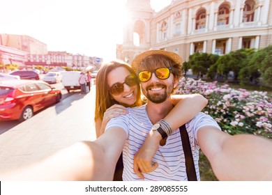 Happy Couple, Attractive Woman And Man Walking  In City And  Enjoying Romance. Lovers Making Selfie, Smiling And Have Fun Together. Odessa, Ukraine.