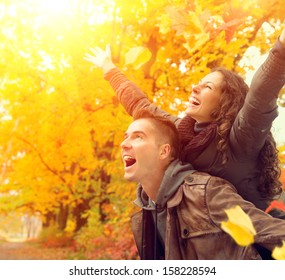 Happy Couple In Autumn Park. Fall. Young Family Having Fun Outdoors. Yellow Trees And Leaves. Laughing Man And Woman Outside. Freedom Concept.