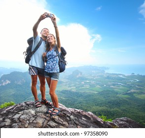 Happy couple with backpacks making a snapshot of themselves on top of a mountain