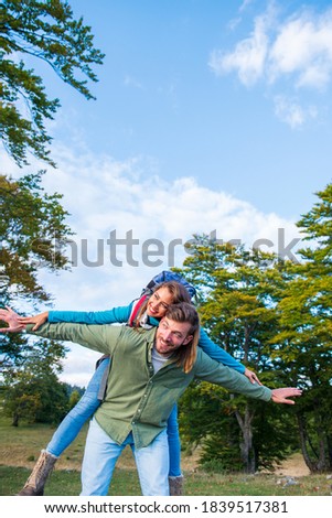 happy couple with backpacks traveling in highlands. Boyfriend carrying his girlfriend on piggyback.