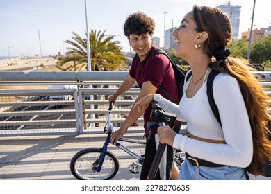 Happy couple in Barcelona going to seaside with bike and scooter - Laughing man and woman walking and pushing bike and electric scooter - Lifestyle, travel and love concepts, hot summer day in Spain - Powered by Shutterstock