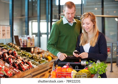 A happy couple buying groceries looking at grocery list on phone - Powered by Shutterstock