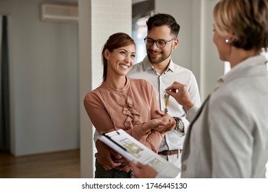 Happy Couple Buying New Home And Receiving House Keys Form Real Estate Agent. 