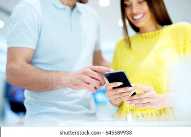 Happy Couple Buying New Smart Phone In Tech Store. Deciding Which Model To Purchase.