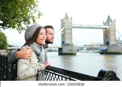 Happy Couple By Tower Bridge, River Thames, London. Romantic Young Couple Enjoying View During Travel. Asian Woman, Caucasian Man In London, England, United Kingdom.