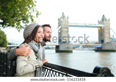 Happy couple by Tower Bridge, River Thames, London. Romantic young couple enjoying view during travel. Asian woman, Caucasian man in London, England, United Kingdom.