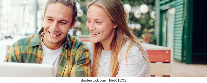 Happy couple in cafe looking at laptop and discussing plans, outdoors. Wide screen - Powered by Shutterstock