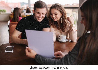 Happy Couple In Cafe Meet With Bussines Woman. Woman Show To Man And Woman Something On Documents