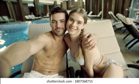 Happy couple calling video online at poolside. Smiling family waving hands in front of mobile camera in slow motion. Young couple having video chat online by pool at luxury spa.