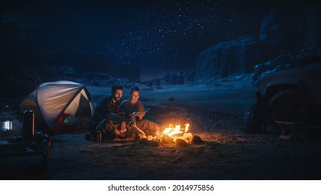 Happy Couple Camping in the Canyon at Night, Use Digital Tablet Computer, Sitting by Campfire. Two people Have Fun, Smile, Post Traveling Photos on Social Media, Watch Funny Videos on Internet - Powered by Shutterstock