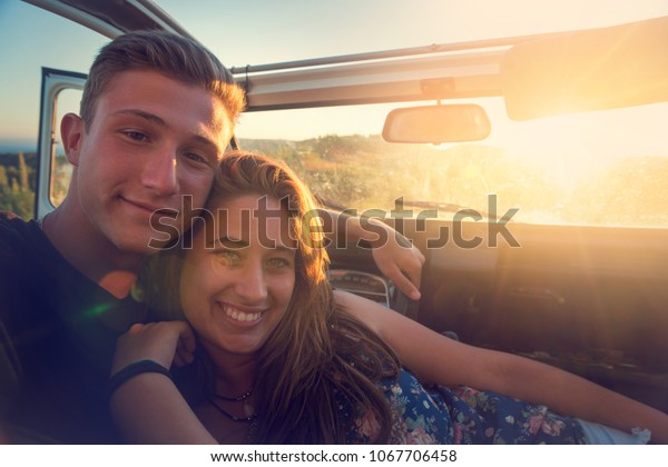 Happy couple in a car\
enjoying sunset.