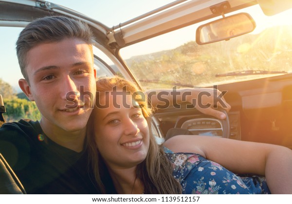 Happy couple in a car\
enjoying sunset.