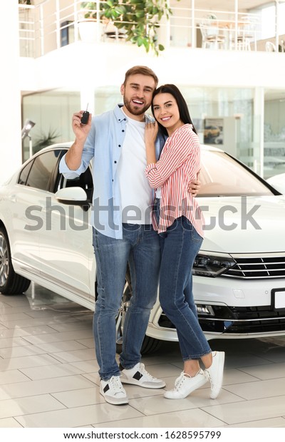 Happy\
couple with car key in modern auto\
dealership