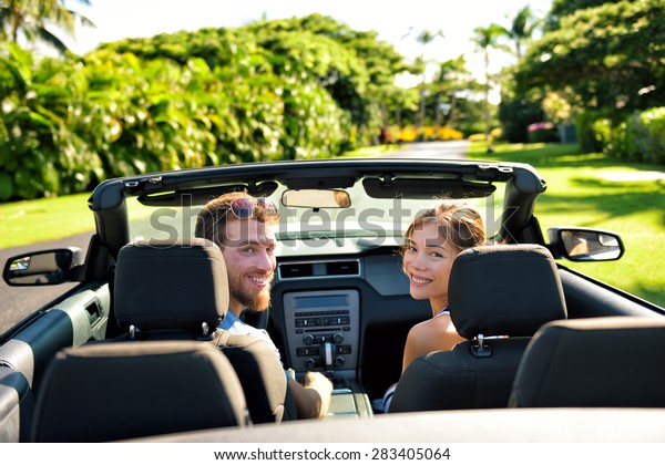 Happy
couple in car on summer road trip travel. Multiracial young couple
carefree on holidays driving a convertible cabriolet automobile on
the roadway in the city looking back at
camera.