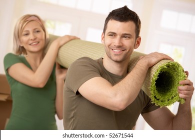 Happy couple carrying carpet together at moving house.