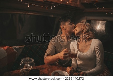 Happy couple celebrating Christmas and New Year winter holidays season in camper. Young couple drinking tea spending time together hugs and kisses in Xmas camper trailer