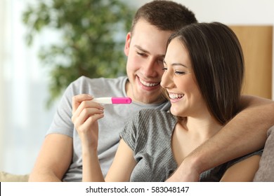 Happy couple checking pregnancy test sitting on a couch in the living room at home