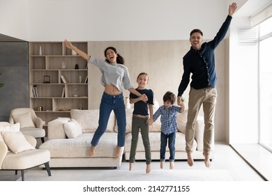 Happy couple and children holding hands jumping barefoot in cozy living room having excited face expression look at camera, celebrate relocation day to own house. Homeowners family moving day concept - Shutterstock ID 2142771155