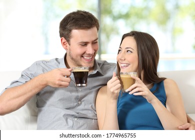 Happy Couple With Coffee Cups Looking At Each Other Sitting In The Sofa At Home