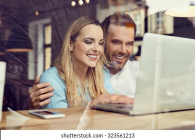 Happy Couple At Coffee Shop Looking At Laptop