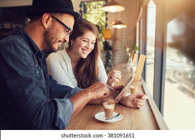 Happy couple in a coffee shop surfing internet on digital tablet. Young man and woman in a restaurant looking at touch screen computer. - Powered by Shutterstock