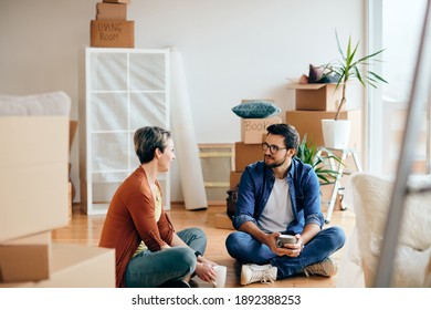 Happy couple communicating while having a cup of coffee and sitting on the floor at their new apartment. 