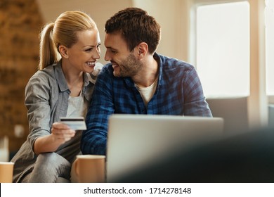 Happy couple communicating while using credit card and laptop for online shopping at home.