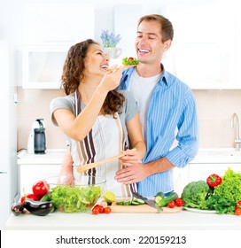 Happy Couple Cooking Together - Man And Woman In Their Kitchen At Home Preparing Dinner - Vegetable Salad. Diet. Dieting. Healthy Vegetarian Food, Vegan. Family Cooking Together At Home