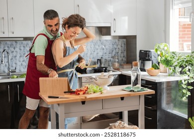 Happy couple cooks together in their modern kitchen, surrounded by fresh vegetables, creating a loving home life - Powered by Shutterstock